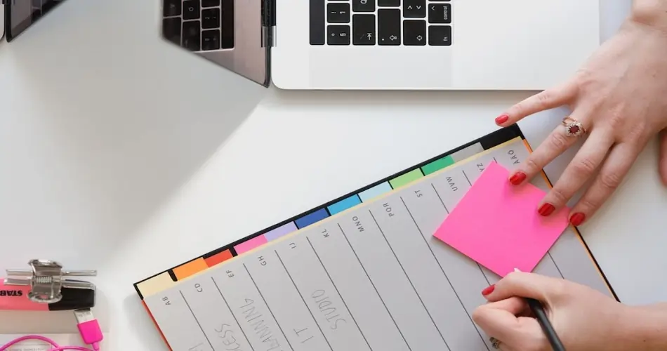 A professional planning content networking services using a to-do list at their desk and writing on a pink Post-It note